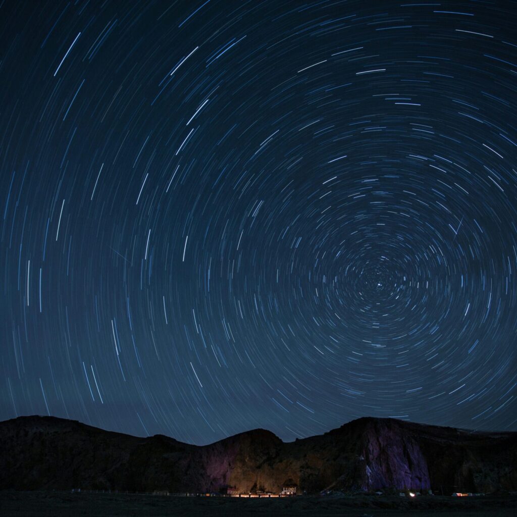 A mesmerizing night sky showcasing rotating star trails over a mountainous landscape.